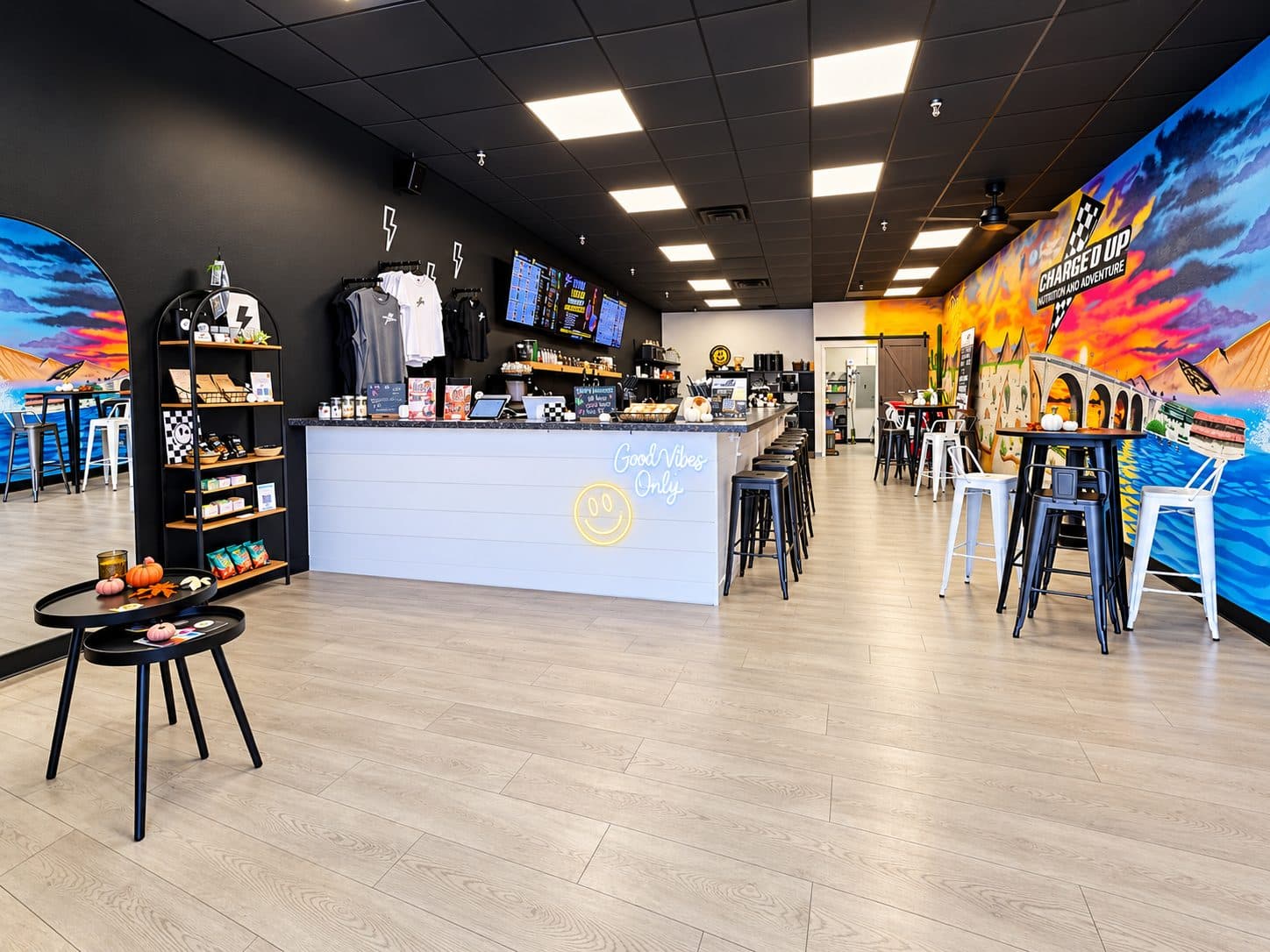 Inside Charged Up Nutrition: the white Good Vibes Only bar with black stools, menu screens and merch shelves, and the colorful Charged Up mural of the London Bridge along the right wall