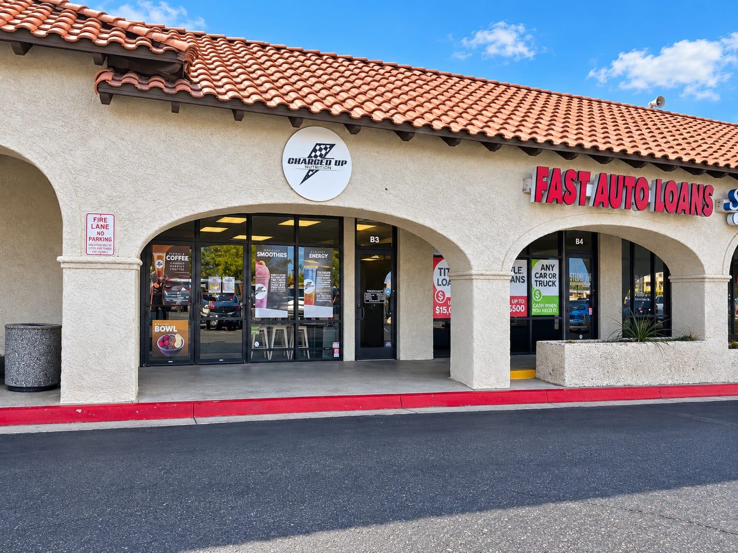 The Charged Up Nutrition storefront on McCulloch Blvd in daylight: white stucco arches, a red tile roof and the round Charged Up sign over the entrance